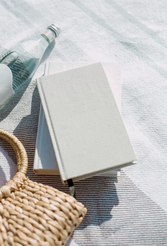 a book, picnic basket and transparent bottle placed on a blanket