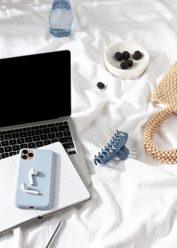 a laptop, phone and bag, and berries and a bottle of water laid on sheet