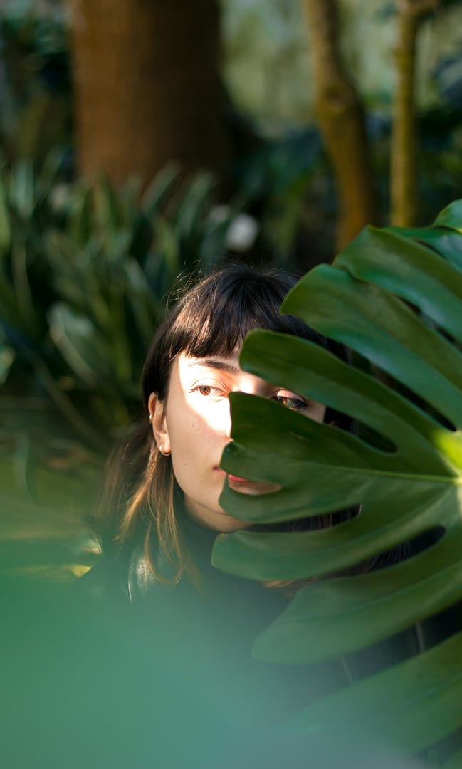 a woman hiding half her face behind a large leaf