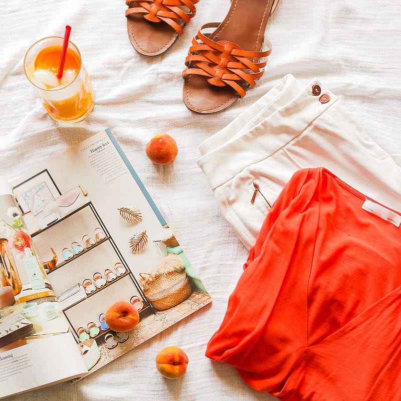 a magazine, shirt and pants and shoes, and a glass of juice laid out on a bed